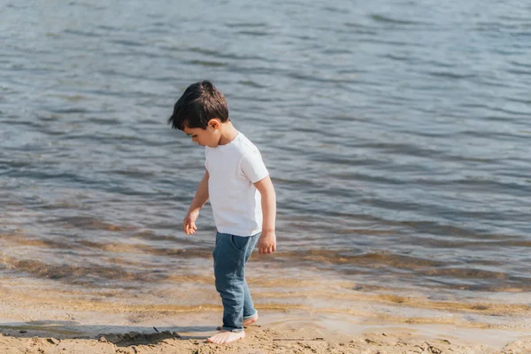 Cute boy in denim jeans standing near blue lake — Stock Photo