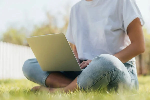Cropped view of freelancer sitting on green grass with laptop — Stock Photo