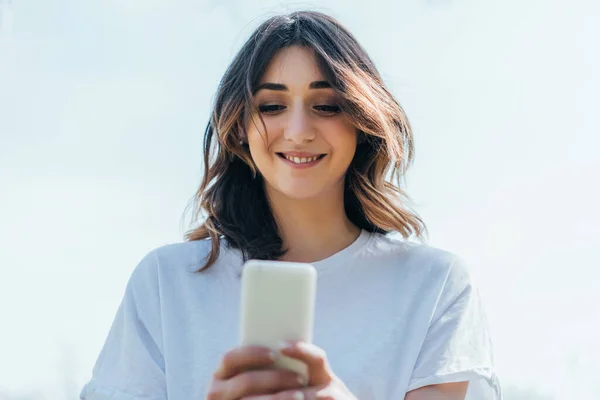 Vista de ángulo bajo de la mujer feliz utilizando el teléfono inteligente fuera - foto de stock