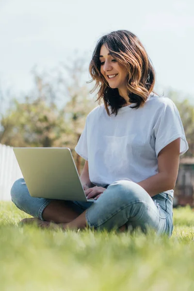 Enfoque selectivo de freelancer feliz usando el ordenador portátil y sentado en la hierba verde - foto de stock