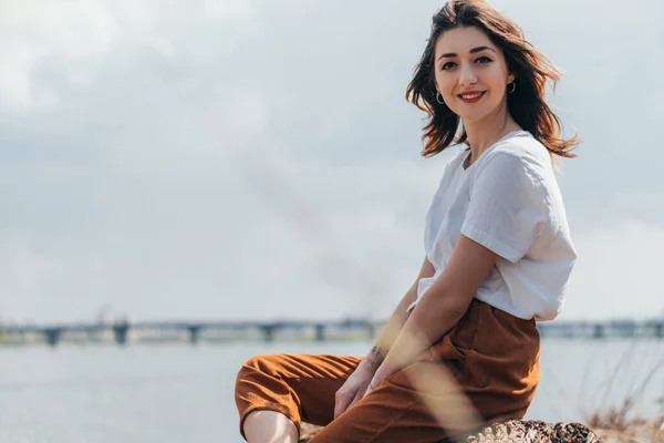 Selective focus of cheerful woman looking at camera near lake — Stock Photo