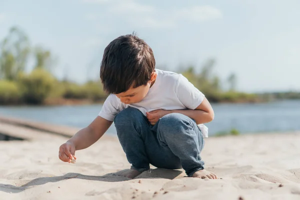 Милый ребенок в джинсах в джинсах сидит и смотрит на песок — стоковое фото