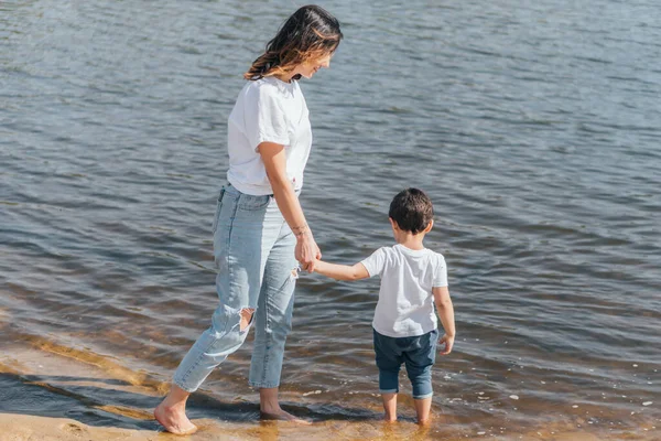 Mère heureuse tenant la main avec un fils mignon et debout dans le lac — Photo de stock