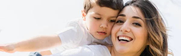 Панорамная концепция веселой матери, смотрящей в камеру рядом с очаровательным сыном — стоковое фото