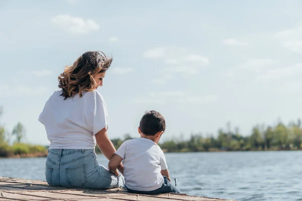Belle mère regardant son fils assis près de la rivière — Photo de stock