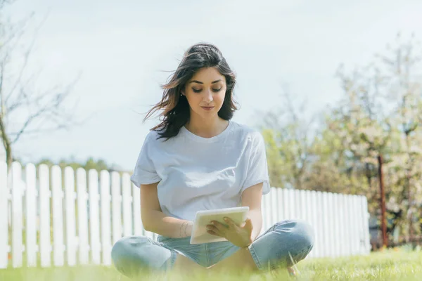 Селективный фокус женщины с помощью цифрового планшета и сидя на траве — стоковое фото