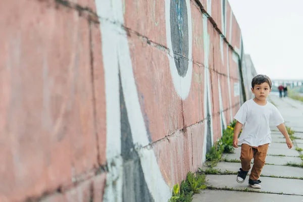 Selective focus of cute boy running near wall with graffiti — Stock Photo