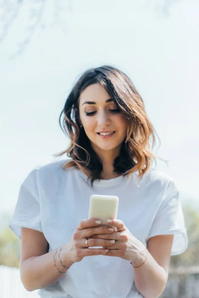 Fröhliche Frau nutzt Smartphone und lächelt draußen — Stockfoto