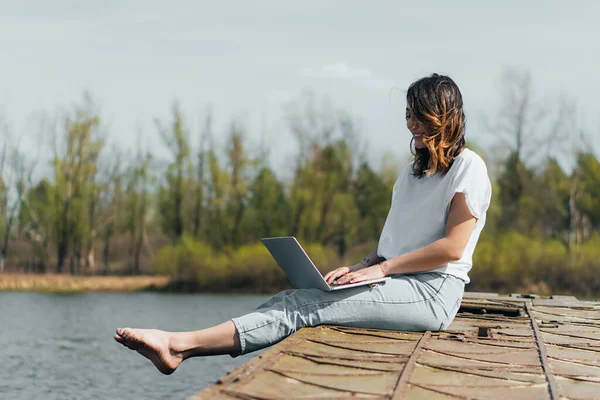 Freelancer alegre usando el ordenador portátil mientras que la creación de redes cerca del lago - foto de stock