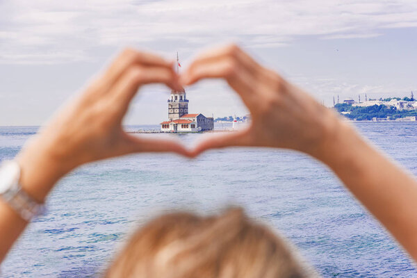 Beautiful woman traveler makes heart shape with hands on view of Maidens Tower,a popular destination in Istanbul,Turkey