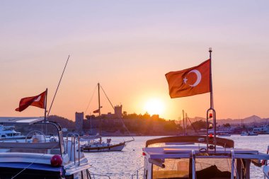 Ön plan, Yatlar ile Bodrum Deniz ve St. Peter Kalesi veya Bodrum Kalesi görünümünü Sunset Bodrum, Türkiye'de arka plan üzerinde Türk bayrağı ile.