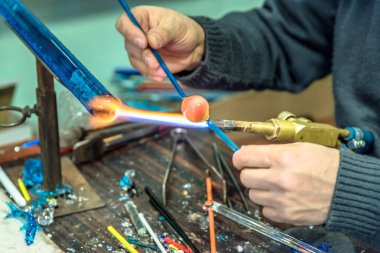 Bir cam konu el sanatları Fuarı'nda yapma el sanatları adamın ellerini. Alev alev yanan bir meşale ile erimiş cam çalışma cam maker. Yeni cam sanat parçası üzerinde lehim lâmbası alev, yakın çekim.