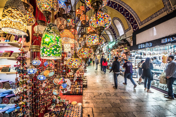 Unidentified people visiting the Grand Bazaar for shopping,.Interior of the Grand Bazaar with traditional handmade decorative mosaic multi-colored Turkish lamps for sale hanging on the front side.Istanbul, Turkey.April 17, 201