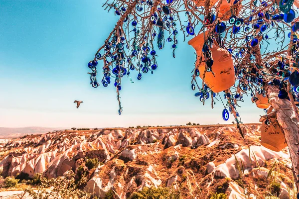 Evil Eye Beads on Tree and Fairy tale chimneys on background of blue sky in Guvercinlik Valley,Goreme,Turkey.Branches of the old tree decorated with the eye-shaped amulets,Nazars,Evil eye,made of blue glass.