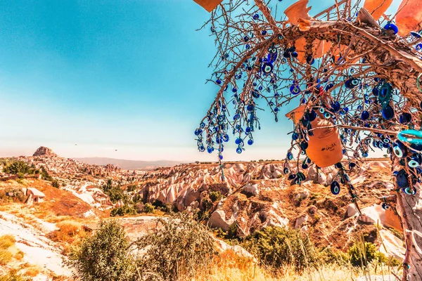 Evil Eye Beads on Tree and Fairy tale chimneys on background of blue sky in Guvercinlik Valley,Goreme,Turkey.Branches of the old tree decorated with the eye-shaped amulets,Nazars,Evil eye,made of blue glass.