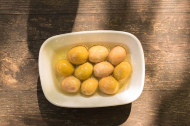 Arka plan doku eski ahşap masa ve bir tabak içinde büyük yeşil zeytin üstten görünüm 