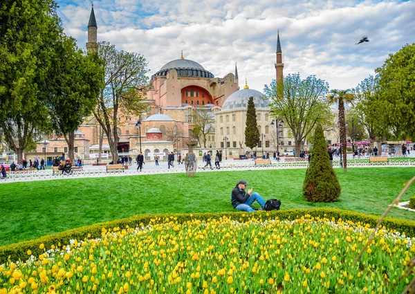 Sultanahmet Meydanı, park, Ayasofya Sophia, bir Yunan Ortodoks Hıristiyan Patriklik Bazilikası'na (kilise) arka plan ve foreground.tourists üzerinde renkli lale manzarasına sahip geleneksel Lale Festivali ziyaret ve zaman harcamak. Türkiye, Istanbul, Nisan 4,2017