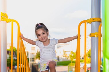 Arkadan yan görünüşü sevimli küçük kız oyun parkında metal merdiven çubuklardan tırmanmaya bağlama 