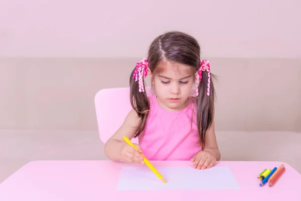 Portrait of Cute girl drawing with colorful pencils on white paper sitting  at table. Selective focus and small depth of field.