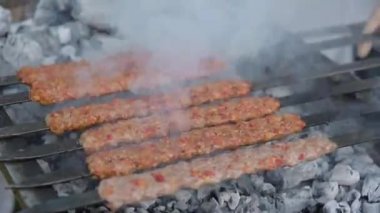 Etten yapılmış çok sayıda çiğ Türk şiş Adana kebabı ızgarada mangal kömürü üzerine dizilmiştir..