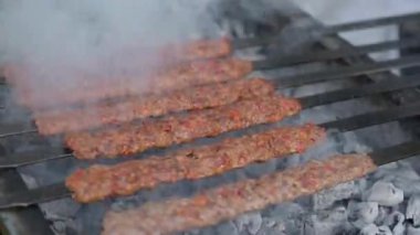 Etten yapılmış çok sayıda çiğ Türk şiş Adana kebabı ızgarada mangal kömürü üzerine dizilmiştir..