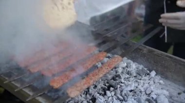 Etten yapılmış çok sayıda çiğ Türk şiş Adana kebabı ızgarada mangal kömürü üzerine dizilmiştir..