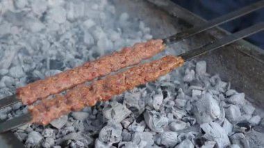 Etten yapılmış çok sayıda çiğ Türk şiş Adana kebabı ızgarada mangal kömürü üzerine dizilmiştir..