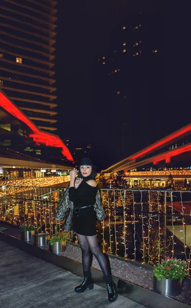 黒の帽子とドレスを持つ魅力的な美しい女性は 背景に都市の照明と夜にポーズ — ストック写真