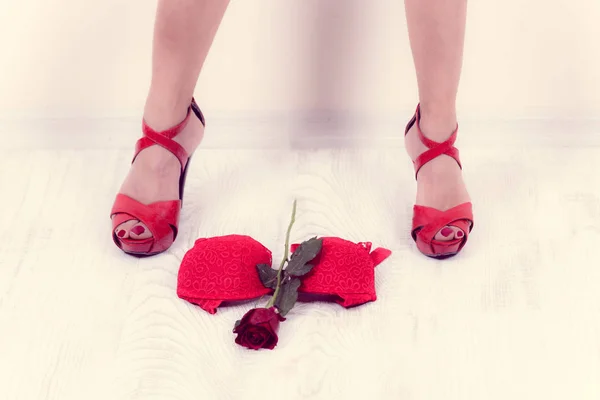 赤いランジェリーとバラは孤立した背景を持つ美しい女性の足の間に立つ — ストック写真