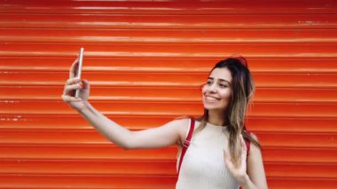 Yavaş hareket: güzel genç kız turuncu önünde akıllı telefon ile selfie alır, kırmızı arka plan