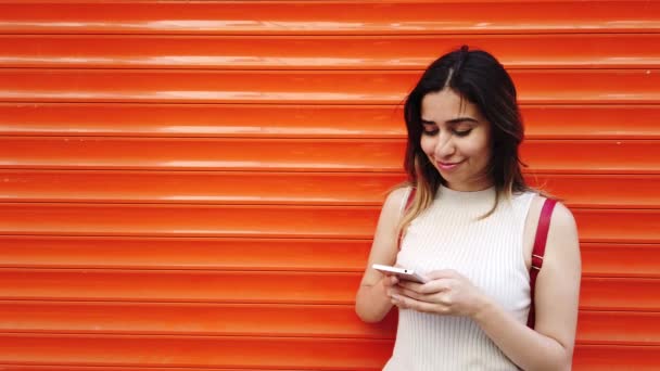 慢动作 美丽的年轻女孩使用智能手机和文本与橙色 红色背景 — 图库视频影像