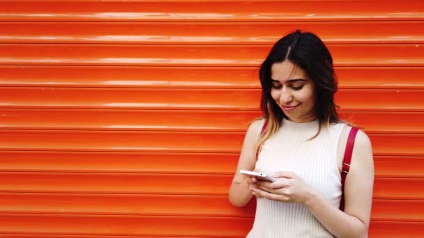 美丽的年轻女孩使用智能手机和文本与橙色 红色背景 — 图库视频影像