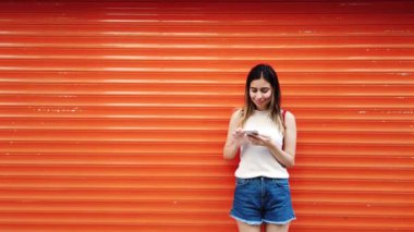 Güzel genç kız turuncu önünde Smartphone kullanır, kırmızı arka plan