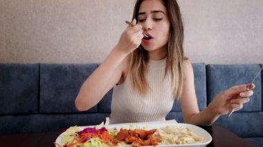 Yavaş hareket: güzel genç kız oturma sırasında bir restoran veya kafede büyük bir zevk ile tavuk yemi yiyor. Gıda konsepti