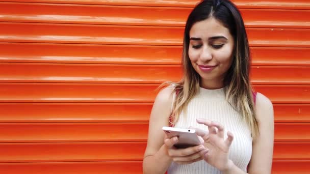 Hermosa Chica Joven Utiliza Teléfono Inteligente Delante Naranja Fondo Rojo — Vídeo de stock
