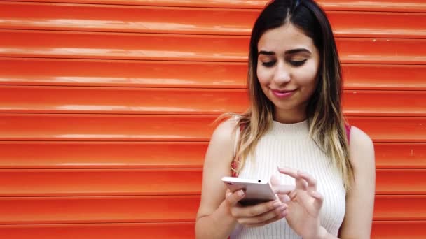 Câmera Lenta Menina Bonita Usa Smartphone Frente Laranja Fundo Vermelho — Vídeo de Stock