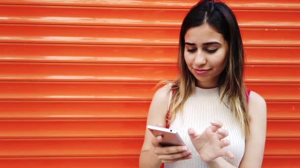 慢动作 美丽的年轻女孩使用智能手机在橙色 红色背景前 — 图库视频影像