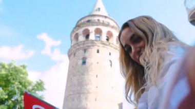 Çekici genç güzel kız, İstanbul'un popüler simge lerinden Galata Kulesi'nin önünde selfie çekiyor ve Türk bayrağı sallıyor.