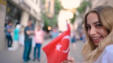 Çekici genç güzel kız Türk bayrağı sallıyor ve İstanbul'da dar sokakta erkek arkadaşının kolunu çekiyor, Türkiye