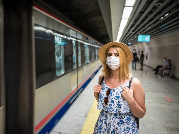 Portrait of young beautiful girl in disposable face mask waits for train on subway platform. Concept of prevention and social distancing in coronavirus,covid19 pandemic