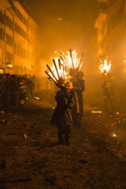 Chienbaese Festivali. İsviçre, Liestal, Rathausstrasse 25, 18 Şubat 2018. Festival katılımcıları yanan süpürge taşıyan eski kasabanın içinden omuzlarında ahşap günlükleri şeklinde.