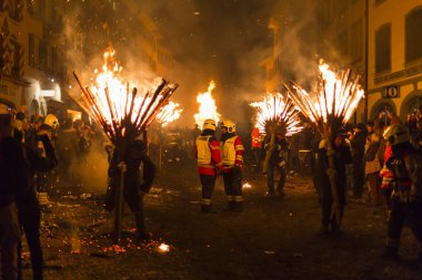 Chienbaese Festivali. İsviçre, Liestal, Rathausstrasse 25, 18 Şubat 2018. Festival katılımcıları yanan süpürge taşıyan eski kasabanın içinden omuzlarında ahşap günlükleri şeklinde.