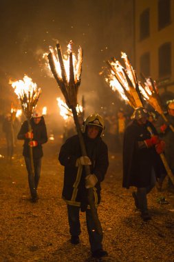 Chienbaese Festivali. İsviçre, Liestal, Rathausstrasse 25, 18 Şubat 2018. Festival katılımcıları yanan süpürge taşıyan eski kasabanın içinden omuzlarında ahşap günlükleri şeklinde.
