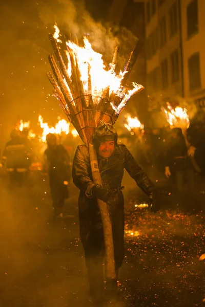 Chienbaese Festivali. İsviçre, Liestal, Rathausstrasse 25, 18 Şubat 2018. Festival katılımcıları yanan süpürge taşıyan eski kasabanın içinden omuzlarında ahşap günlükleri şeklinde.
