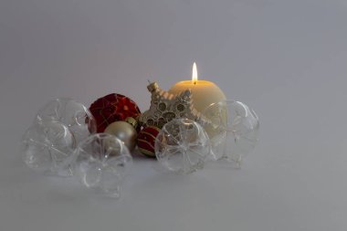 Natürmort güzel dekoratif şeffaf ve kırmızı Noel cam topları, yuvarlak saten renkli yanan muma ve gri arka plan üzerinde saten bir yıldız süs