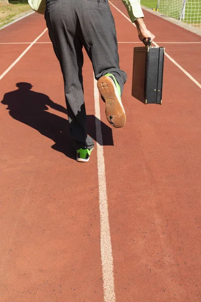 A business man in gray suit with green shirt, black briefcase and broken green sports shoes running on a running track.
