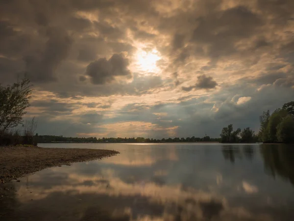 Gün batımında, bulutların arasından parlayan yapraklara doğal sahilinde ile gölde uzun pozlama