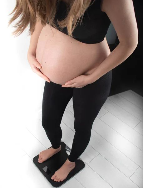 Pregnant woman measures her weight gain in pregnancy on weight scale. Healthy diet eating concept. Slim young skinny fit lady girl model posing on white background