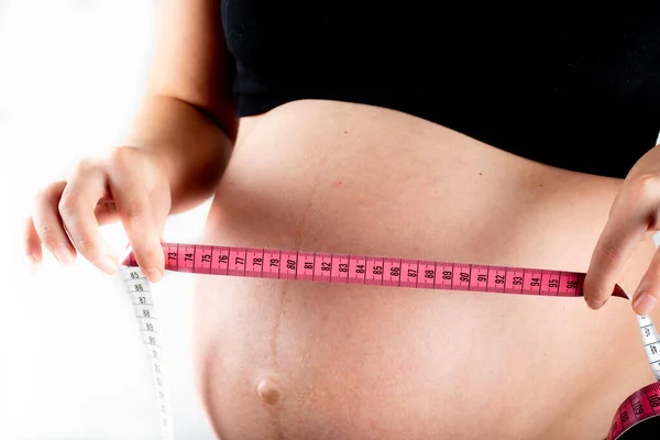 Young pregnant woman measures her waist with measurement tape, weight diet and healthy lifestyle pregnancy concept. Black top and leggings isolated model on white background