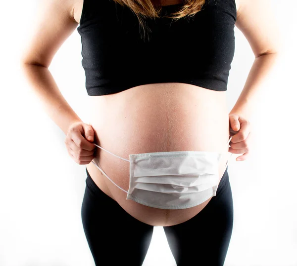 Pregnant woman holding white medicinal face mask on her pregnant belly abdomen. Coronavirus covid19 new normal rules and regulations, isolation and new lifestyle concept